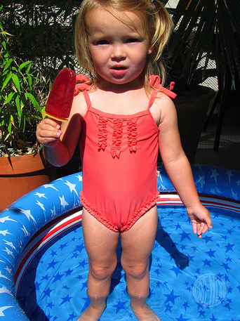 Young girl eating a popsicle standing in a wading pool