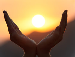 Hands cupped to hold distant sun setting over mountains