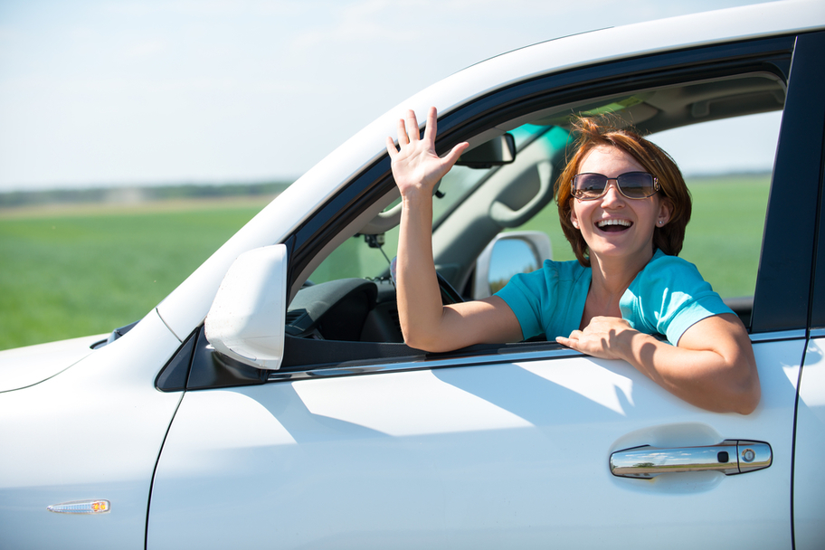 Smiling woman waving at you from her car