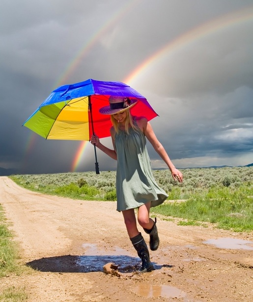 Young woman puddle splashing with rainbow in background